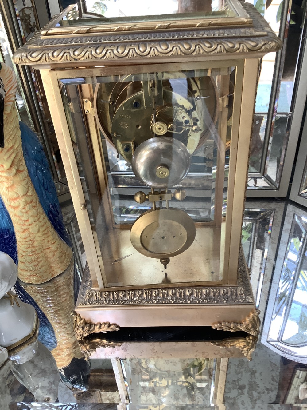A 19th-century French four-glass mantel clock featuring a gilt brass case with decorative moulding, bevelled glass panels, a white enamel dial with Roman numerals, and a visible mercury pendulum. View VI