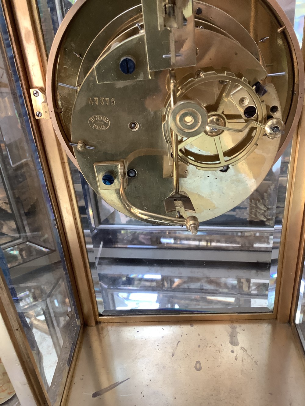 A 19th-century French four-glass mantel clock featuring a gilt brass case with decorative moulding, bevelled glass panels, a white enamel dial with Roman numerals, and a visible mercury pendulum. View X