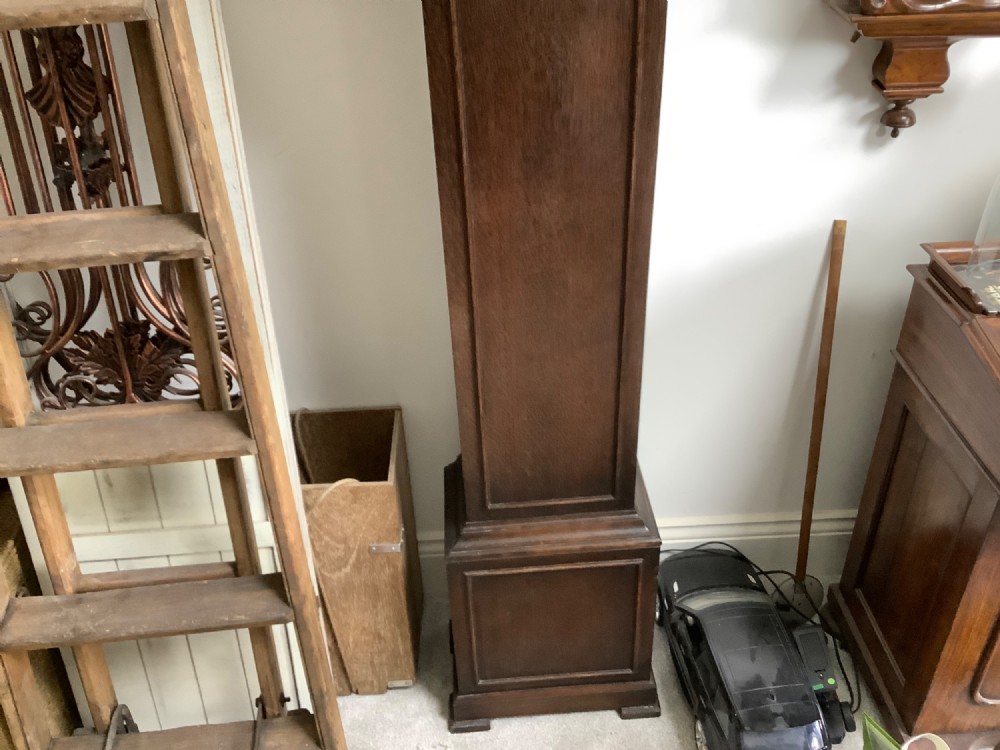 A dark oak freestanding grandmother clock with a pointed arched hood, glass door, and a brass dial featuring chime selection sub-dials. View IV