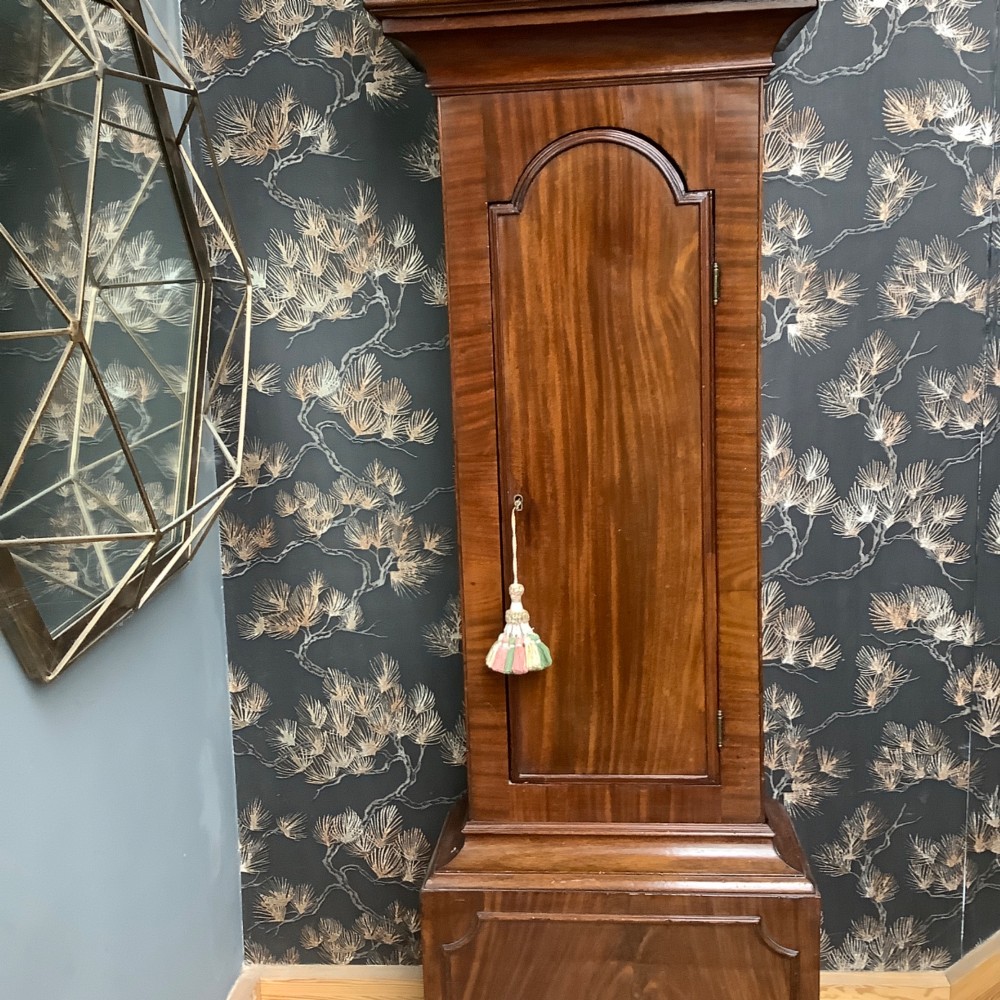 An antique mahogany grandfather clock featuring a painted dial with Roman numerals, a swan-neck pediment, reeded columns, and a polished timber trunk door. View II