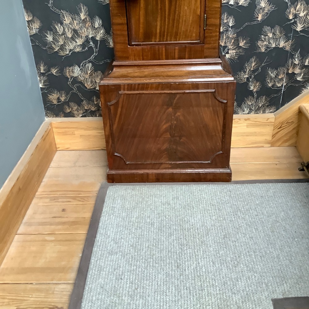 An antique mahogany grandfather clock featuring a painted dial with Roman numerals, a swan-neck pediment, reeded columns, and a polished timber trunk door. View VI