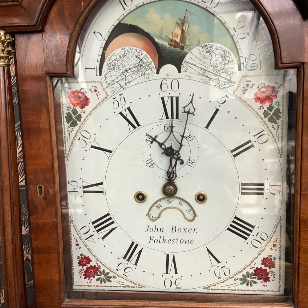 An antique mahogany grandfather clock featuring a painted dial with Roman numerals, a swan-neck pediment, reeded columns, and a polished timber trunk door. View VIII