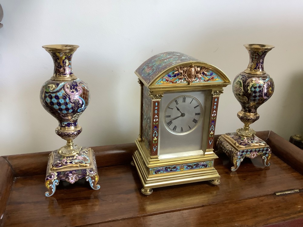 A three-piece French champleve enamel clock garniture set featuring an arched central clock flanked by two matching ornamental vases on gilt bases.
