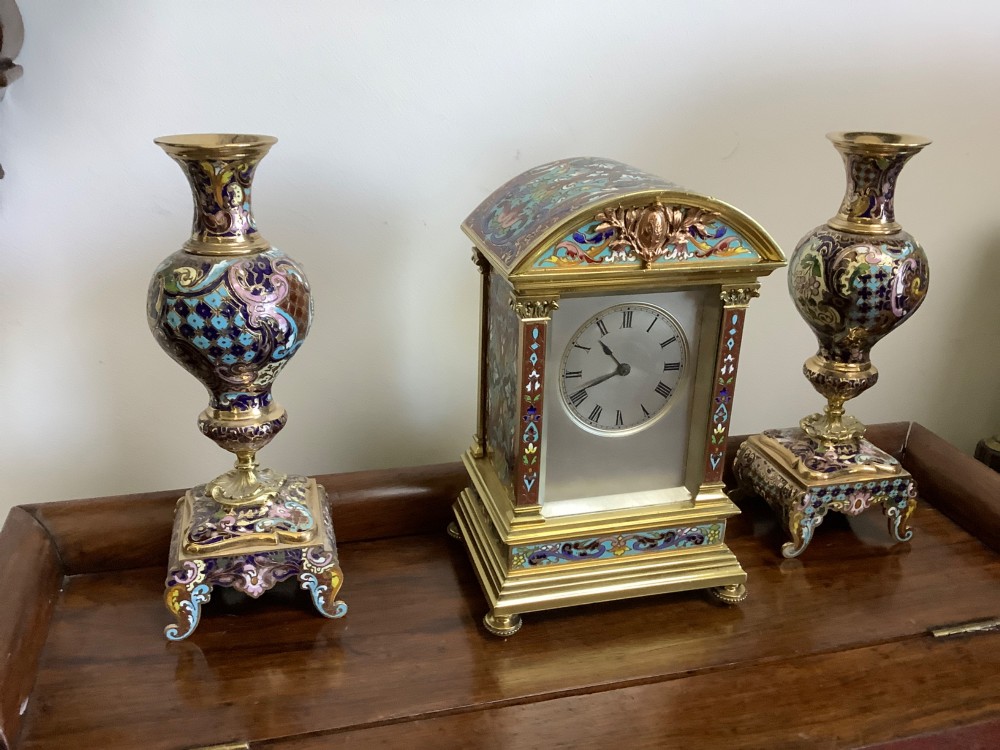 A three-piece French champleve enamel clock garniture set featuring an arched central clock flanked by two matching ornamental vases on gilt bases. View II