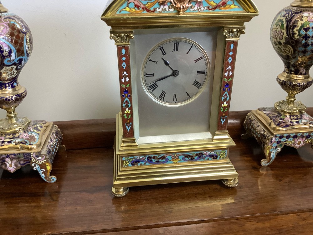 A three-piece French champleve enamel clock garniture set featuring an arched central clock flanked by two matching ornamental vases on gilt bases. View III