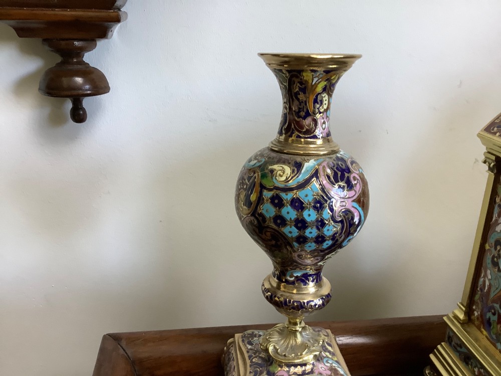 A three-piece French champleve enamel clock garniture set featuring an arched central clock flanked by two matching ornamental vases on gilt bases. View V