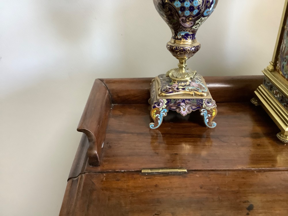 A three-piece French champleve enamel clock garniture set featuring an arched central clock flanked by two matching ornamental vases on gilt bases. View VII