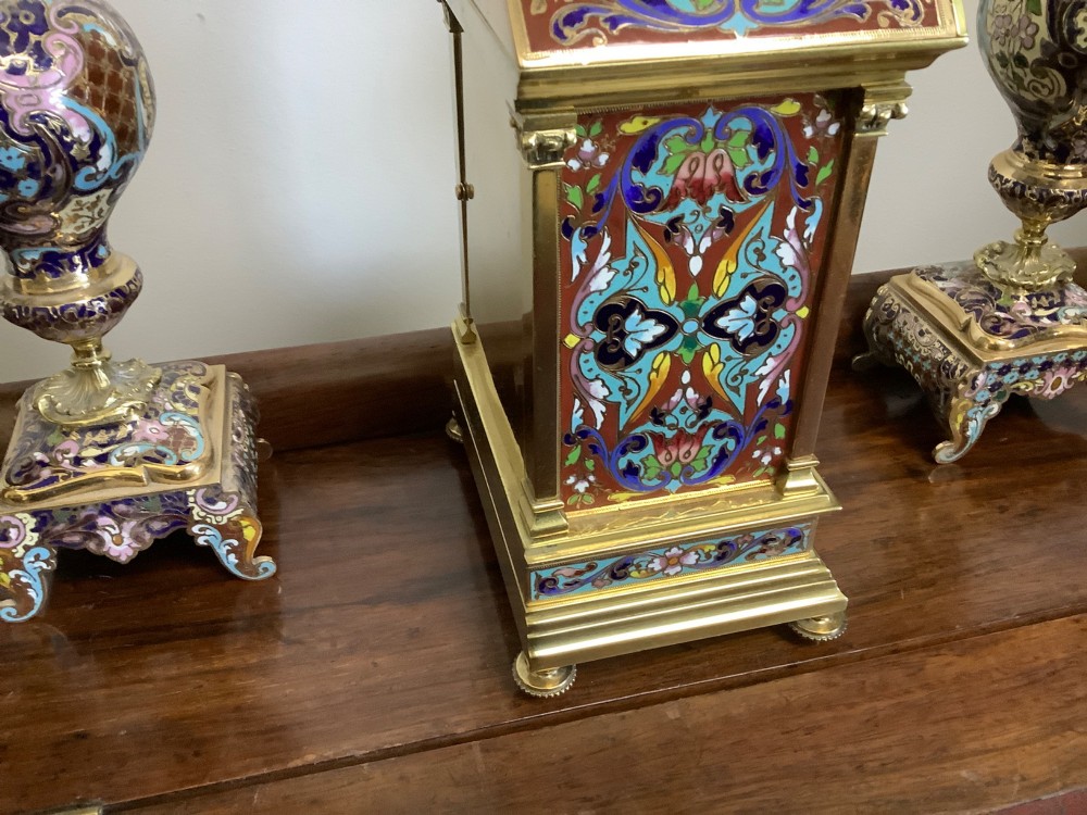 A three-piece French champleve enamel clock garniture set featuring an arched central clock flanked by two matching ornamental vases on gilt bases. View IX