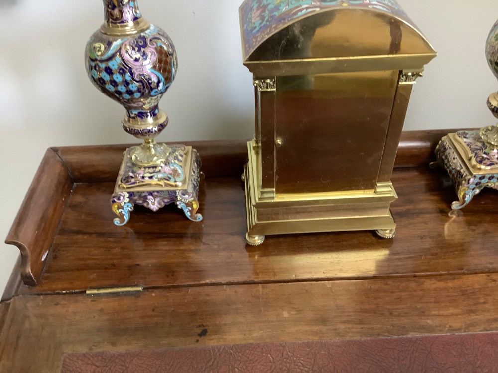A three-piece French champleve enamel clock garniture set featuring an arched central clock flanked by two matching ornamental vases on gilt bases. View XII