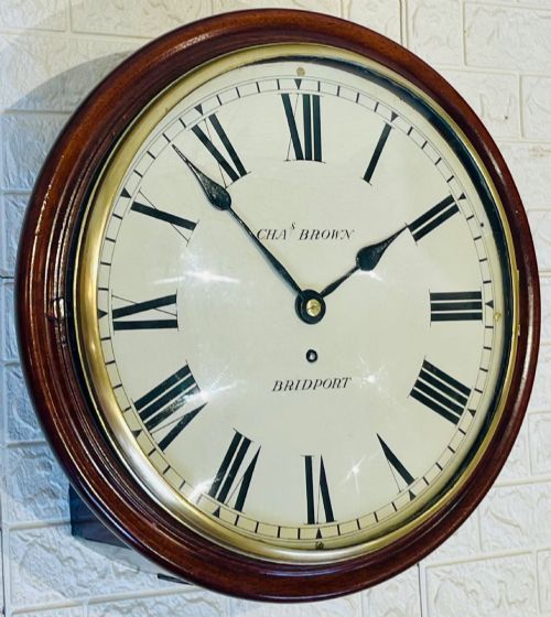 fig 1. A circular Georgian fusee wall clock with a dark mahogany frame, a cream painted dial with Roman numerals, and a polished brass bezel.
