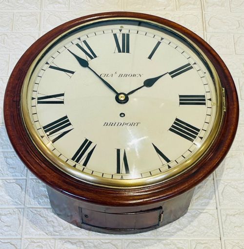 fig 2. A circular Georgian fusee wall clock with a dark mahogany frame, a cream painted dial with Roman numerals, and a polished brass bezel.