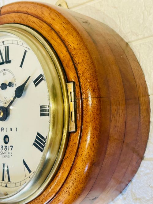 fig 3. A circular vintage British Rail wall clock featuring a warm brown wooden casing, a hinged brass bezel, and a white dial with black Roman numerals stamped B.R.(E) Smiths Empire.