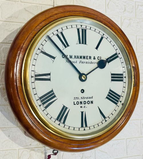 fig 1. A circular Victorian mahogany wall clock featuring a white dial with black Roman numerals, a polished brass bezel, and London maker inscription.