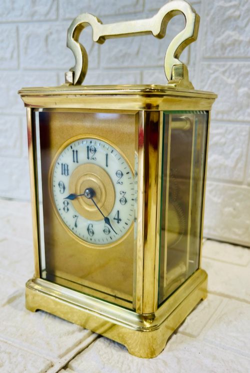 fig 1. A French brass carriage clock featuring a top carrying handle, clear glass viewing panels, and a white enamel dial with black numerals.