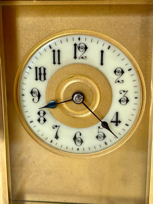 fig 2. A French brass carriage clock featuring a top carrying handle, clear glass viewing panels, and a white enamel dial with black numerals.