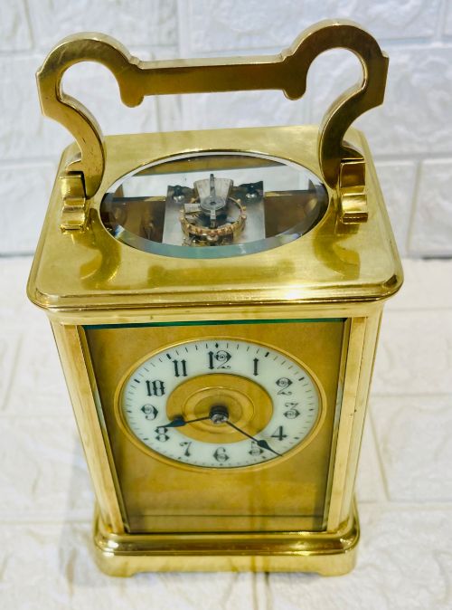 fig 3. A French brass carriage clock featuring a top carrying handle, clear glass viewing panels, and a white enamel dial with black numerals.
