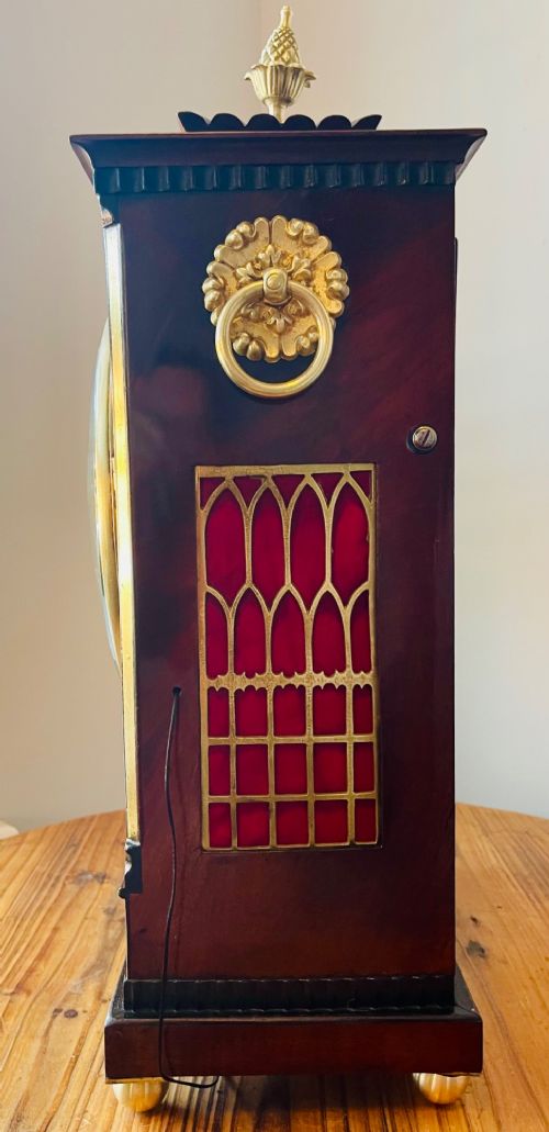 An antique Regency dark mahogany bracket clock featuring intricate brass inlay scrollwork, a brass pineapple finial, side brass lion-mask drop handles, and a cream dial with Roman numerals. View X