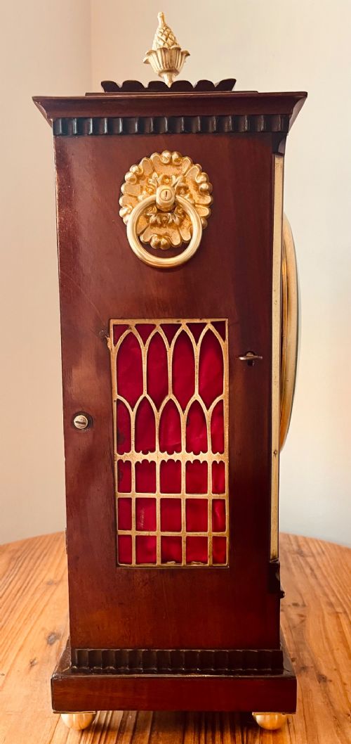 An antique Regency dark mahogany bracket clock featuring intricate brass inlay scrollwork, a brass pineapple finial, side brass lion-mask drop handles, and a cream dial with Roman numerals. View XIV