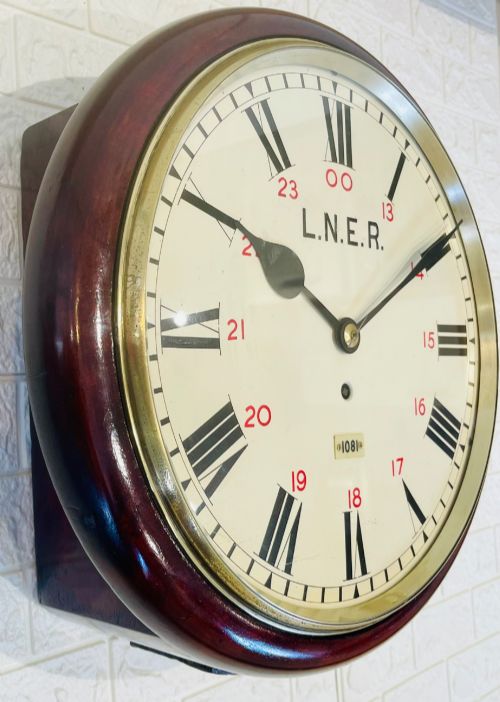 fig 1. A circular LNER fusee railway wall clock featuring a dark mahogany wooden surround, brass bezel, cream dial with black Roman numerals and red 24-hour numbers.