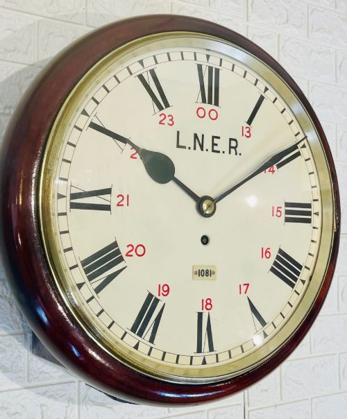 fig 2. A circular LNER fusee railway wall clock featuring a dark mahogany wooden surround, brass bezel, cream dial with black Roman numerals and red 24-hour numbers.