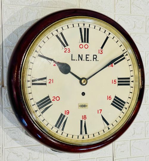 fig 3. A circular LNER fusee railway wall clock featuring a dark mahogany wooden surround, brass bezel, cream dial with black Roman numerals and red 24-hour numbers.