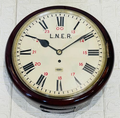 fig 5. A circular LNER fusee railway wall clock featuring a dark mahogany wooden surround, brass bezel, cream dial with black Roman numerals and red 24-hour numbers.