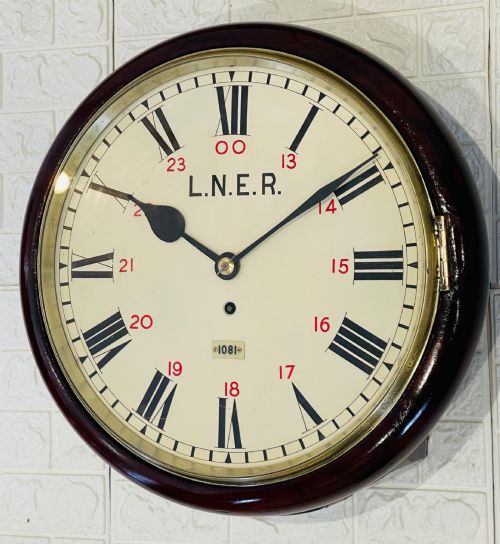 fig 6. A circular LNER fusee railway wall clock featuring a dark mahogany wooden surround, brass bezel, cream dial with black Roman numerals and red 24-hour numbers.