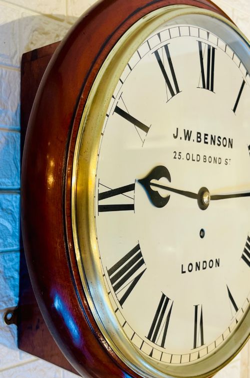 fig 1. A circular mahogany fusee wall clock featuring a white dial face with black Roman numerals, brass bezel, and J. W. Benson London markings.