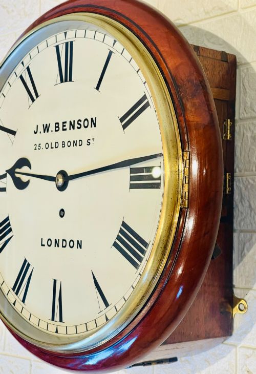 fig 2. A circular mahogany fusee wall clock featuring a white dial face with black Roman numerals, brass bezel, and J. W. Benson London markings.