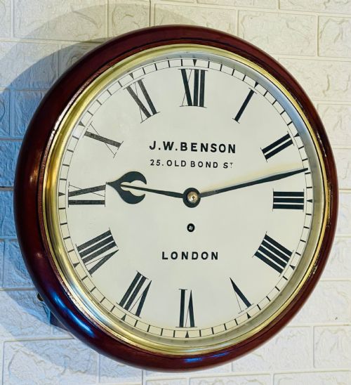 fig 5. A circular mahogany fusee wall clock featuring a white dial face with black Roman numerals, brass bezel, and J. W. Benson London markings.