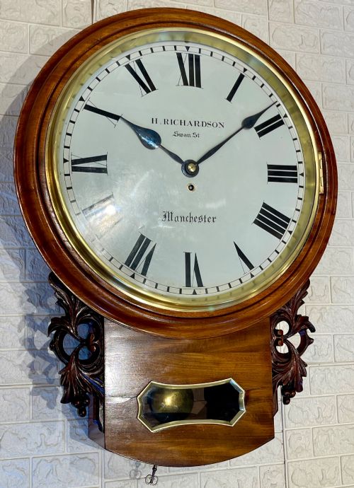 fig 3. Victorian oak drop dial wall clock featuring a circular white dial with Roman numerals, a brass bezel, and carved side scrolls.