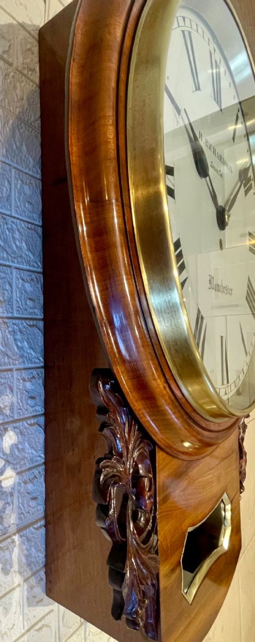 Victorian oak drop dial wall clock featuring a circular white dial with Roman numerals, a brass bezel, and carved side scrolls. View VIII