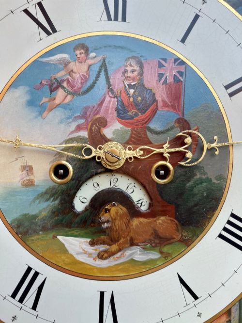 fig 1. A tall Regency mahogany longcase clock featuring a swan-neck hood pediment, brass finial, fluted columns, and a hand-painted dial with figurative scenes.