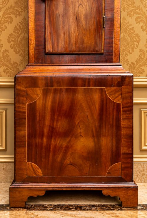 fig 3. A tall Regency mahogany longcase clock featuring a swan-neck hood pediment, brass finial, fluted columns, and a hand-painted dial with figurative scenes.