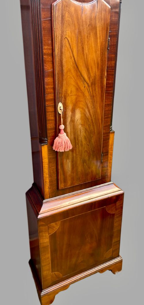 fig 8. A tall Regency mahogany longcase clock featuring a swan-neck hood pediment, brass finial, fluted columns, and a hand-painted dial with figurative scenes.