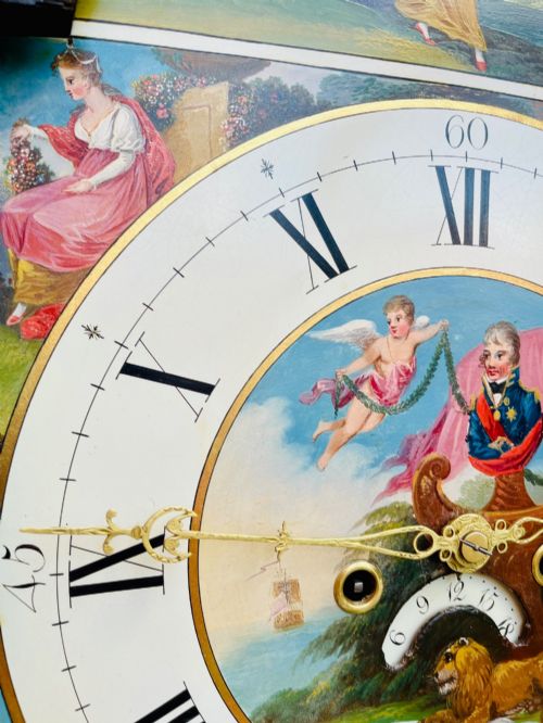 fig 9. A tall Regency mahogany longcase clock featuring a swan-neck hood pediment, brass finial, fluted columns, and a hand-painted dial with figurative scenes.