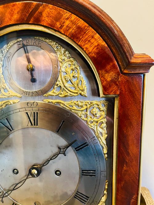 fig 1. A George III mahogany bracket clock featuring an arched case with a brass top handle, gilt spandrels, and a silvered dial.