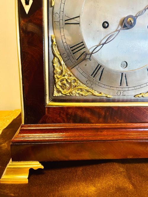 fig 2. A George III mahogany bracket clock featuring an arched case with a brass top handle, gilt spandrels, and a silvered dial.