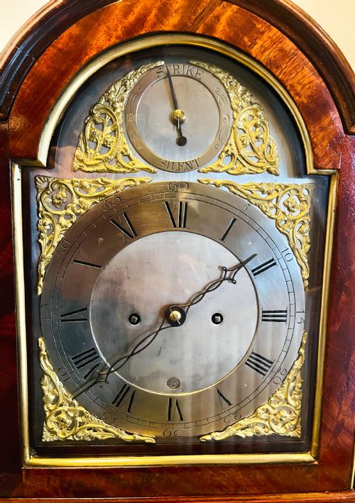 fig 3. A George III mahogany bracket clock featuring an arched case with a brass top handle, gilt spandrels, and a silvered dial.