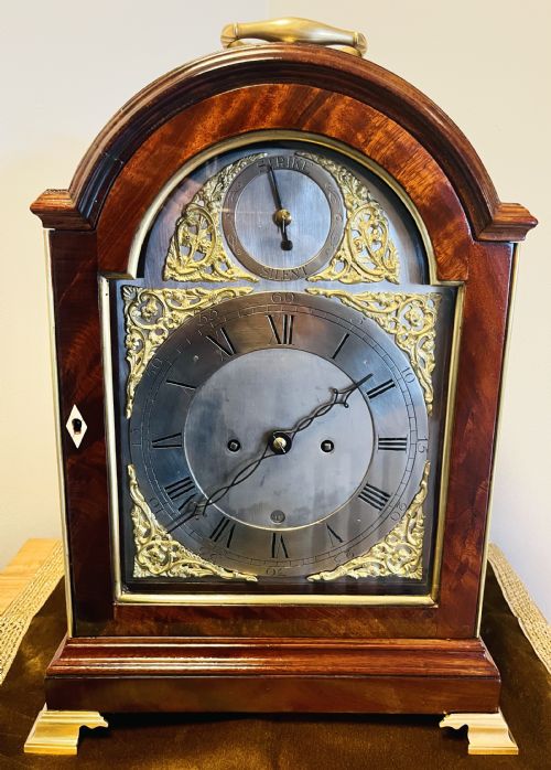 fig 4. A George III mahogany bracket clock featuring an arched case with a brass top handle, gilt spandrels, and a silvered dial.