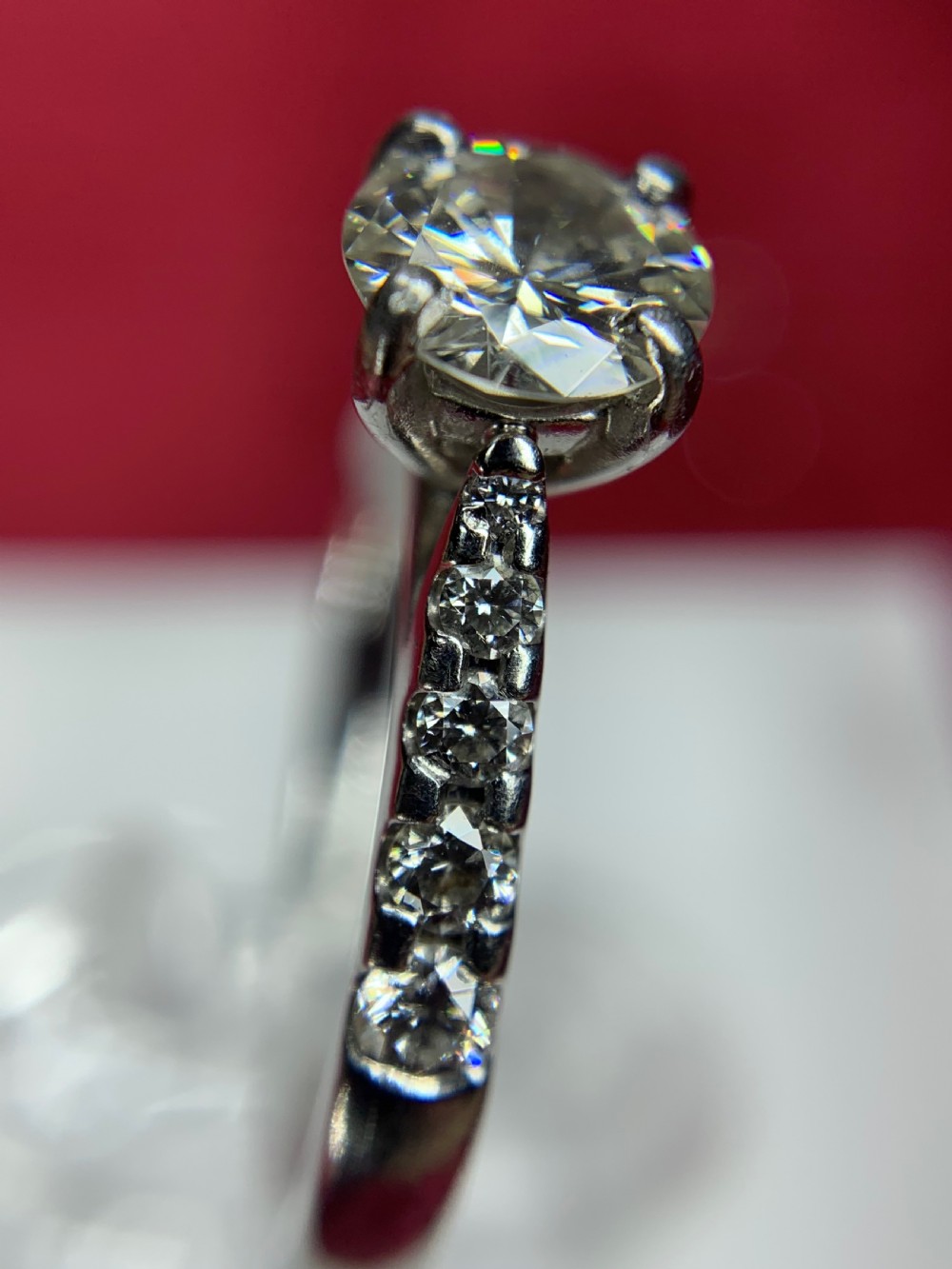 A platinum solitaire engagement ring featuring a central round brilliant-cut diamond in a four-claw setting with diamond-accented shoulders. View X