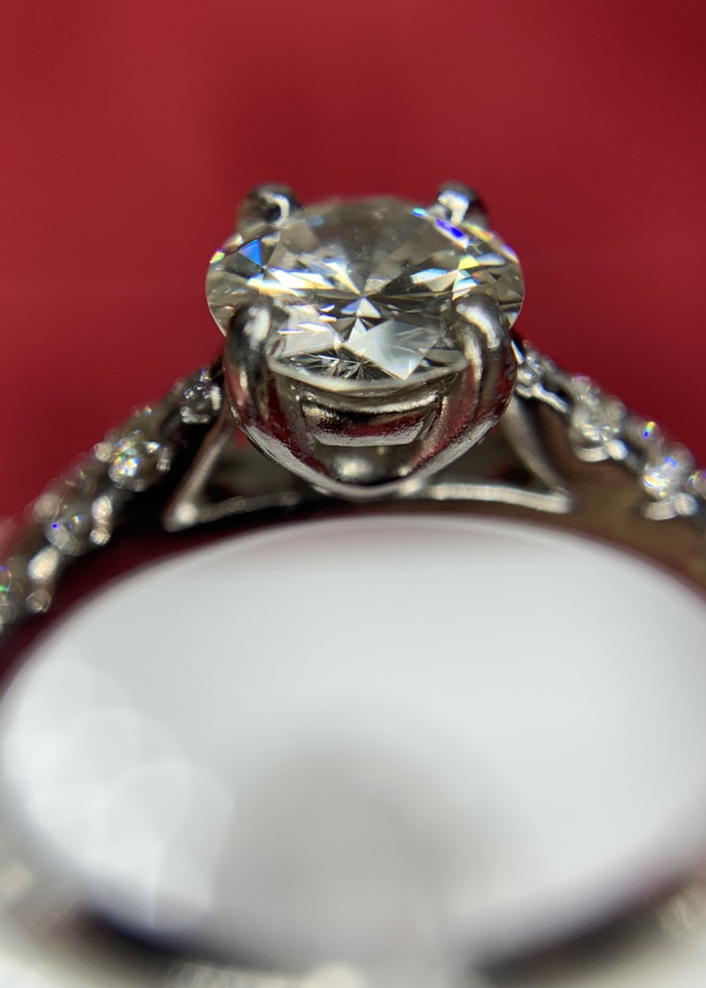 A platinum solitaire engagement ring featuring a central round brilliant-cut diamond in a four-claw setting with diamond-accented shoulders. View XI