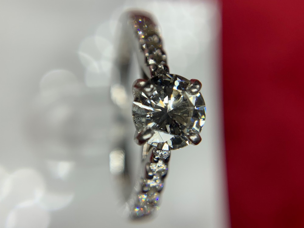A platinum solitaire engagement ring featuring a central round brilliant-cut diamond in a four-claw setting with diamond-accented shoulders. View XIII