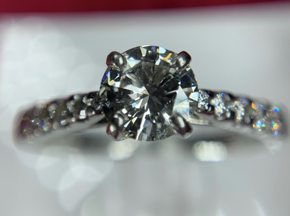 A platinum solitaire engagement ring featuring a central round brilliant-cut diamond in a four-claw setting with diamond-accented shoulders. View XIV