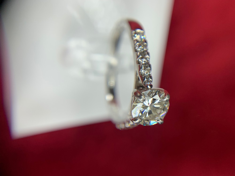 A platinum solitaire engagement ring featuring a central round brilliant-cut diamond in a four-claw setting with diamond-accented shoulders. View XVII
