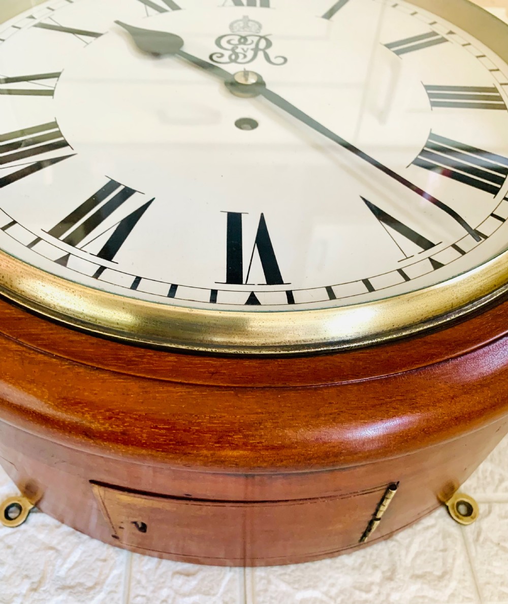 A circular antique fusee wall clock featuring a warm mahogany wooden surround, a brass glass bezel, and a white painted dial with black Roman numerals and a GVR royal cypher monogram. View VIII