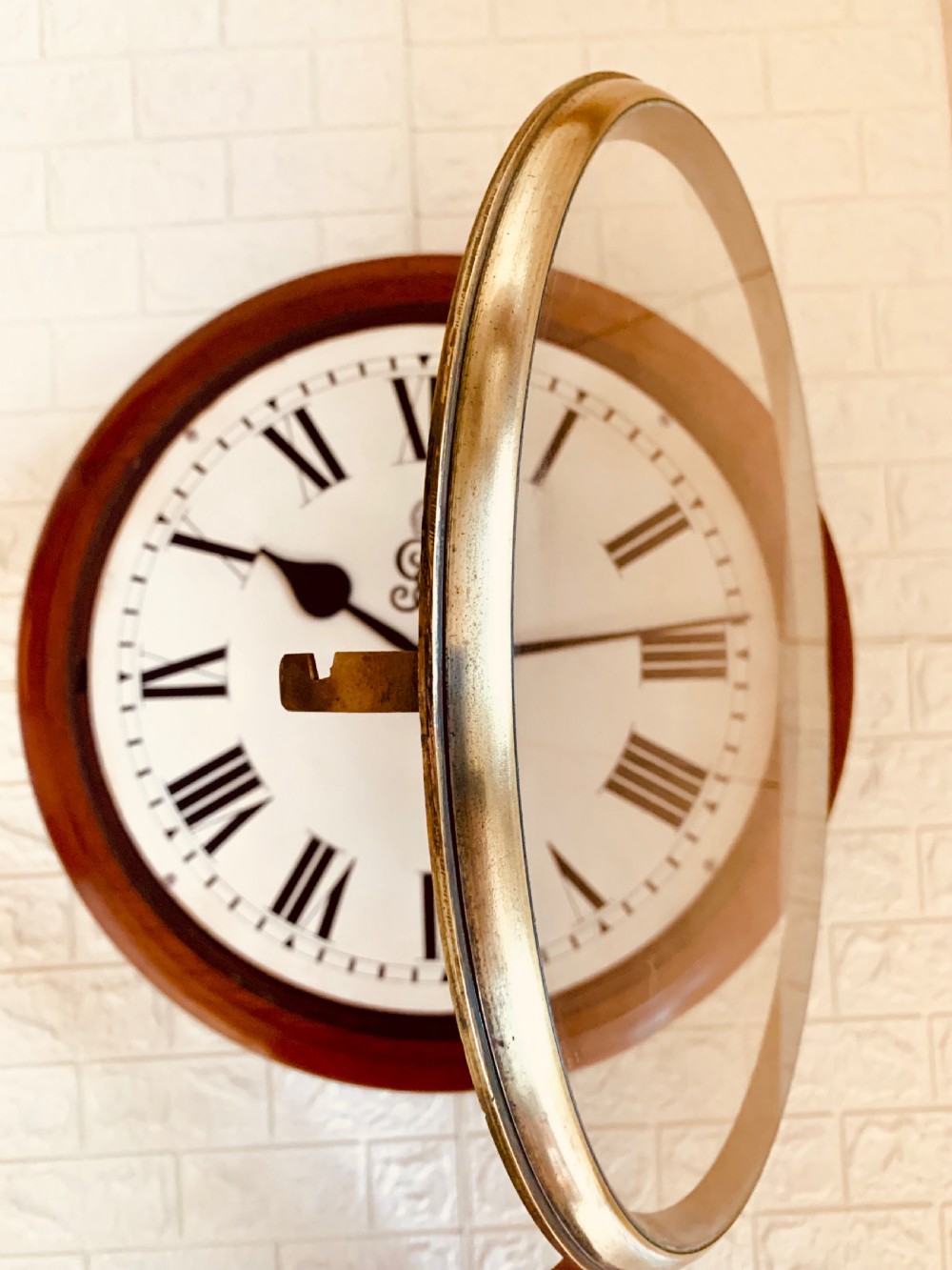 A circular antique fusee wall clock featuring a warm mahogany wooden surround, a brass glass bezel, and a white painted dial with black Roman numerals and a GVR royal cypher monogram. View XII