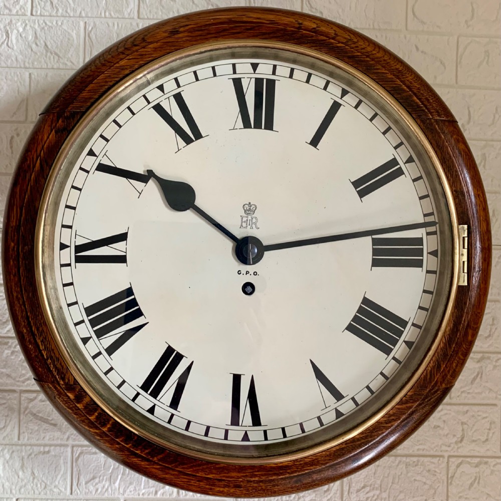 A circular wooden wall clock with a white dial, Roman numerals, black hands, and official G.P.O. markings set within a brass bezel. View II