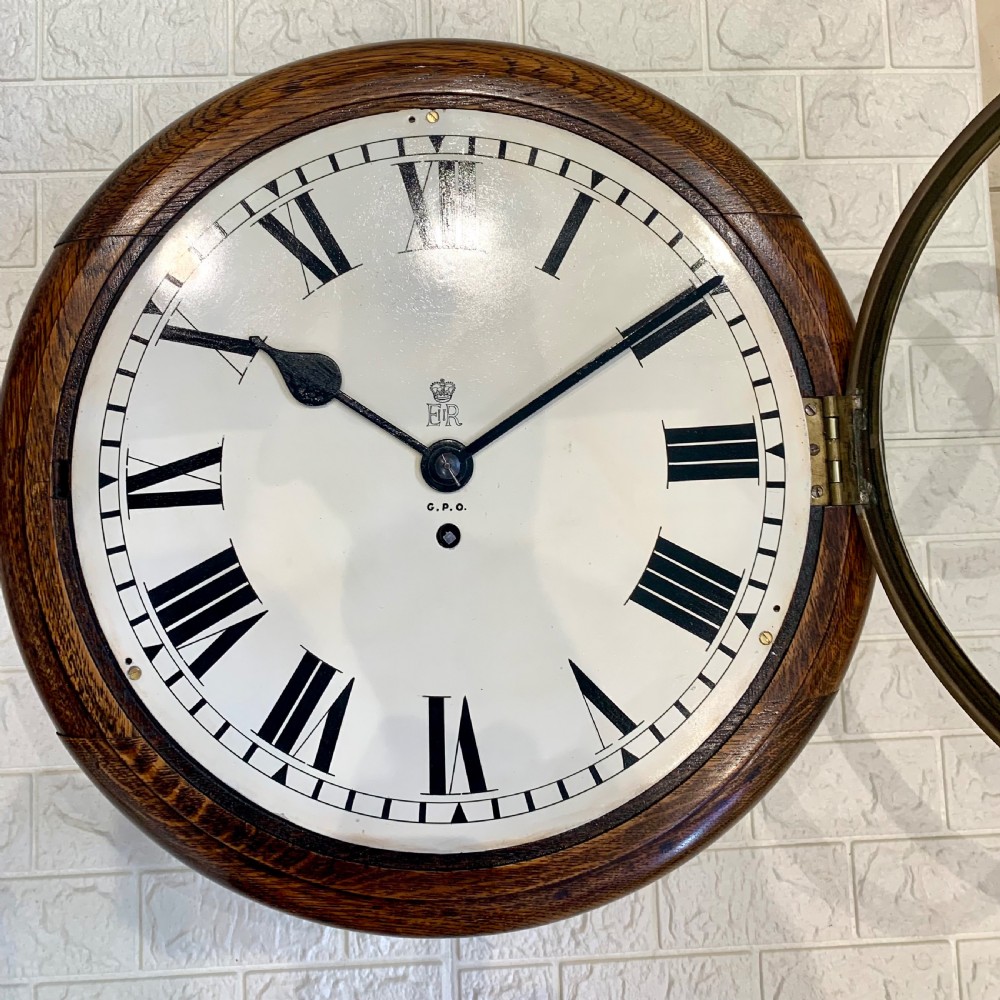 A circular wooden wall clock with a white dial, Roman numerals, black hands, and official G.P.O. markings set within a brass bezel. View IV