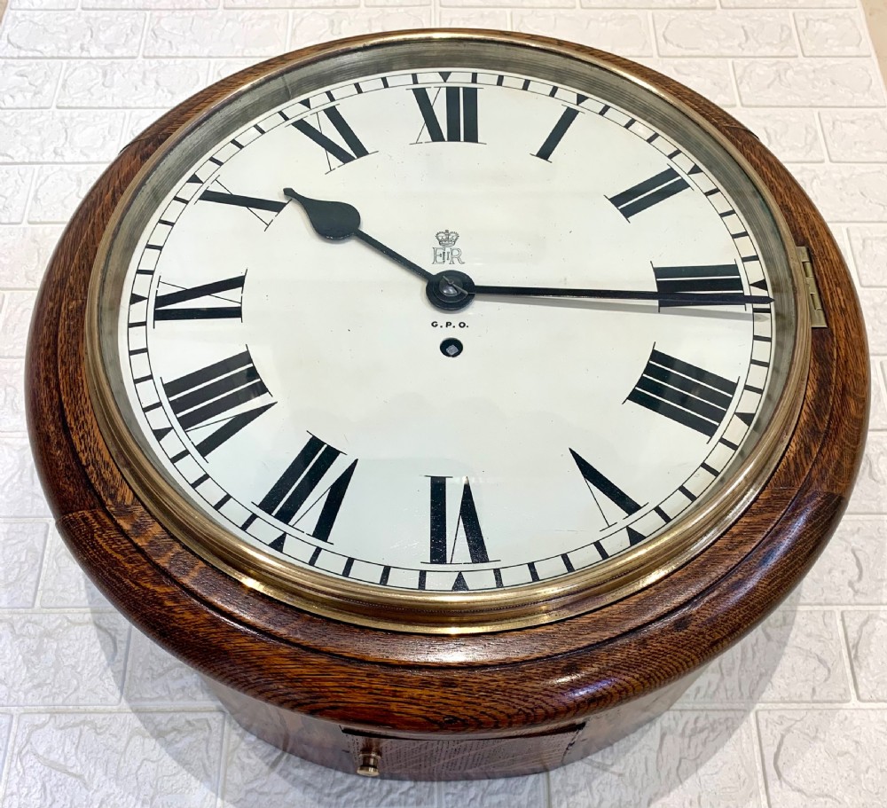 A circular wooden wall clock with a white dial, Roman numerals, black hands, and official G.P.O. markings set within a brass bezel. View VI